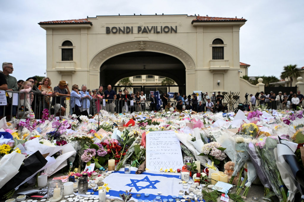 People stand near flowers laid as a tribute at Bondi Beach to honour the victims of a mass shooting that targeted a Hanukkah celebration at Bondi Beach on Sunday, in Sydney, Australia, December 16, 2025. REUTERS/Flavio Brancaleone